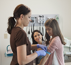 Healthcare provider preparing to take blood sample from girl, while mother watches